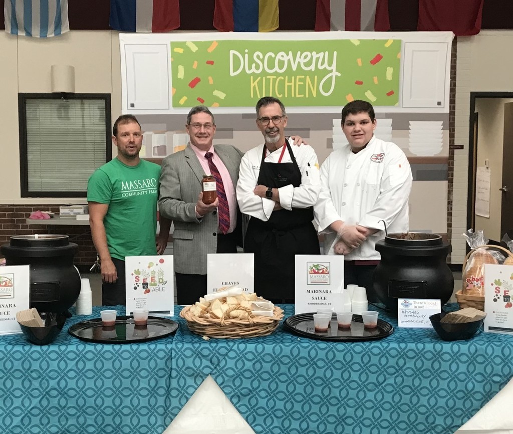 Students and teachers posing with marinara sauces and chips in the discovery kitchen