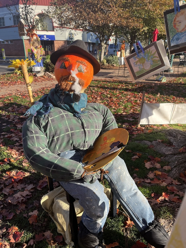 An artist scarecrow with a painted pumpkin for a head, holding a paint palette 