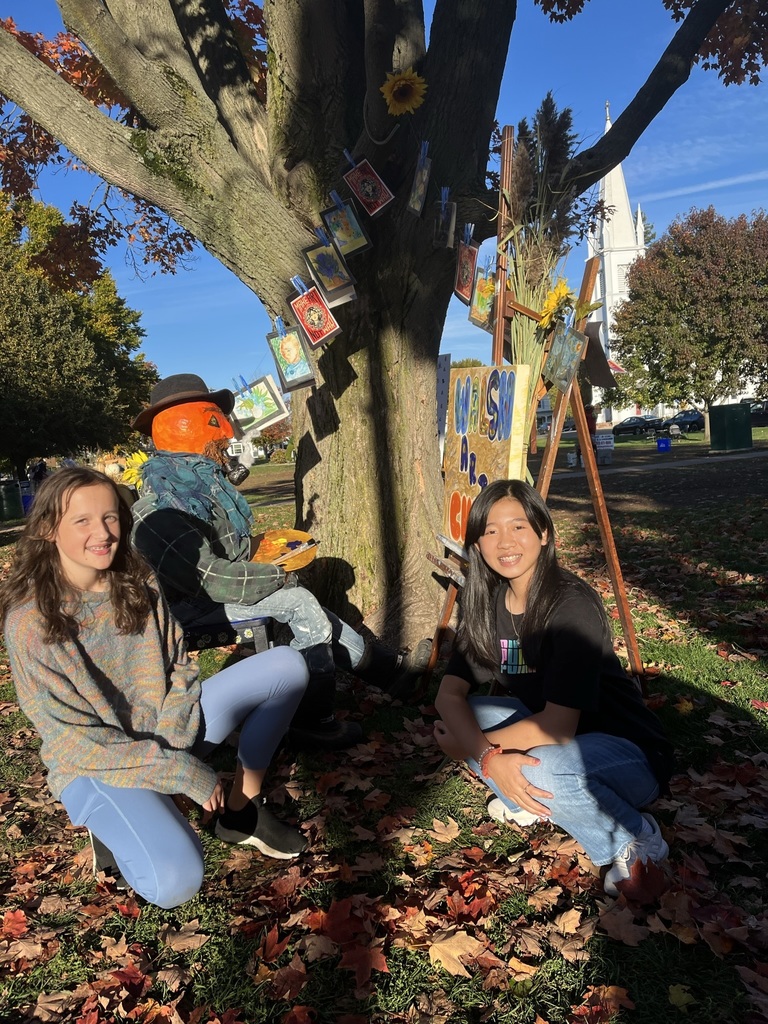 Students posing with hand made signs and paintings in front of a tree