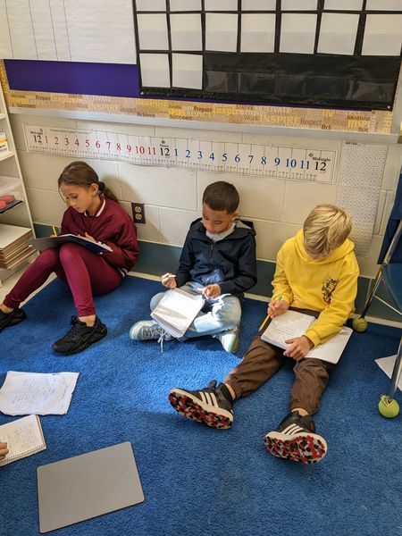 Students sitting on classroom floor writing in their notebooks