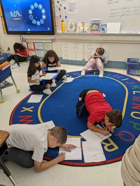 Students sitting on rug writing in their notebooks